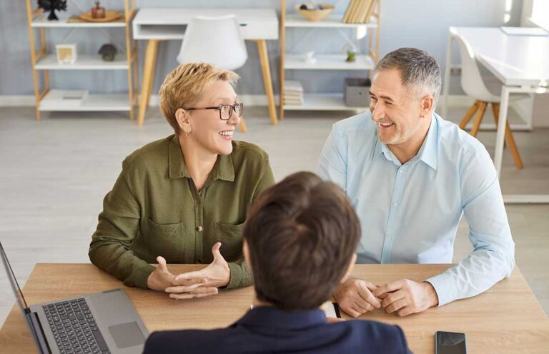 A middle-aged adult and an elderly parent reviewing paperwork at a kitchen table together.